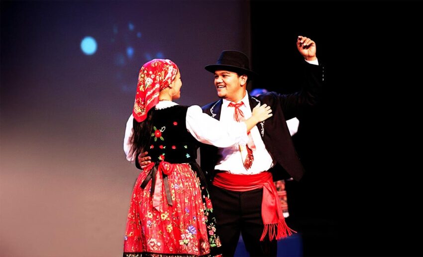 A man and woman in vibrant traditional Kristang costumes performing a lively Branyo dance at the San Pedro Festival in Melaka.