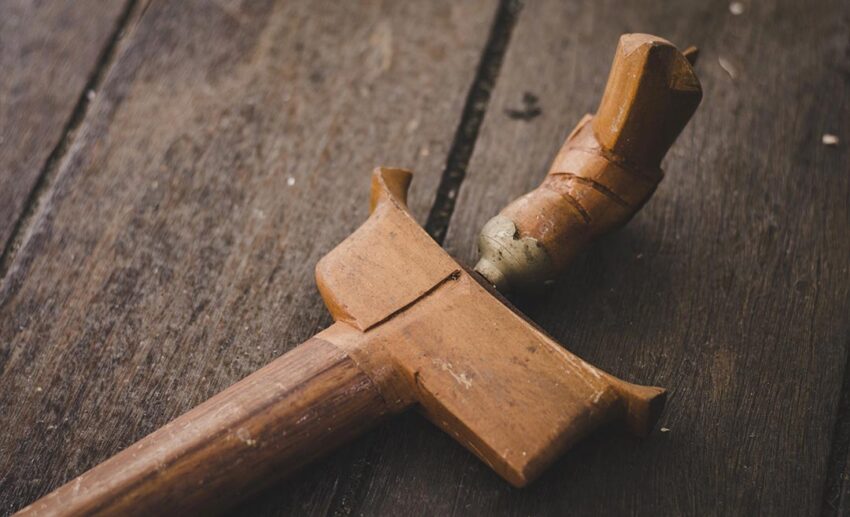 A traditional Malaysian Keris with a carved wooden handle and matching sheath, showcasing the intricate metalwork of the asymmetrical blade.