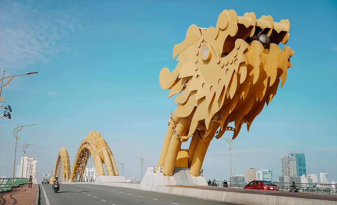A daytime view of the golden Dragon Bridge (Cau Rong) spanning the River Han in Da Nang, Vietnam, under a clear blue sky.