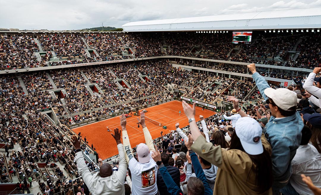 A high-angle view of the packed spectator seats and the clay court at the Roland-Garros tennis tournament in Paris during a 2026 match.